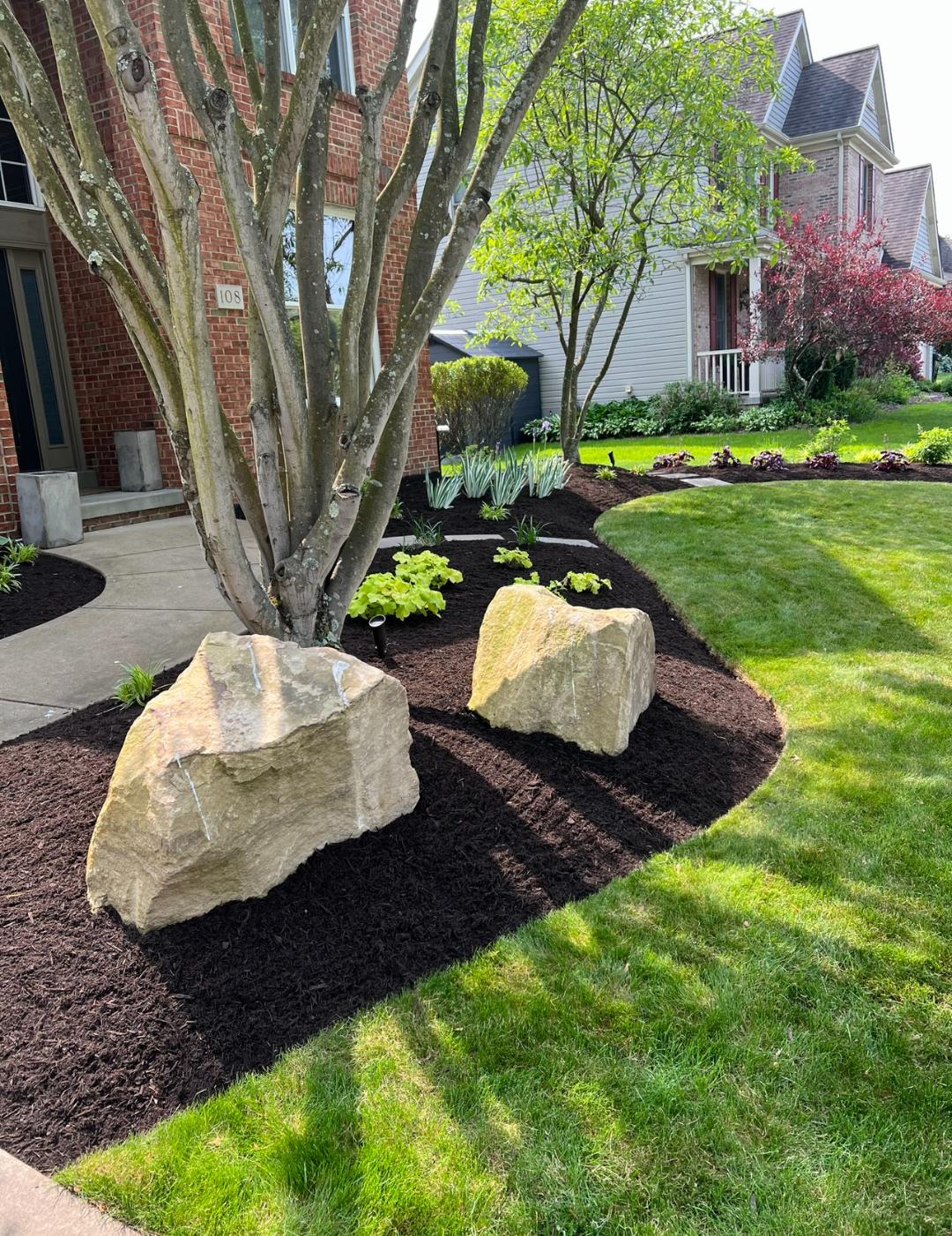 Finished residential landscape with specimen boulders, curved mulch beds, trees, shrubs, and lawn