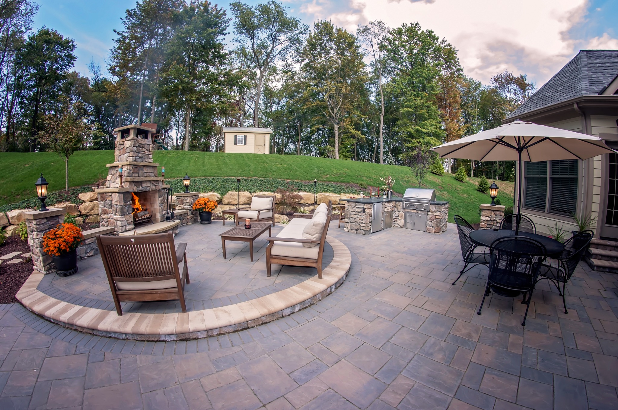 Custom paver patio with stone fireplace, outdoor kitchen, seating, and dining areas